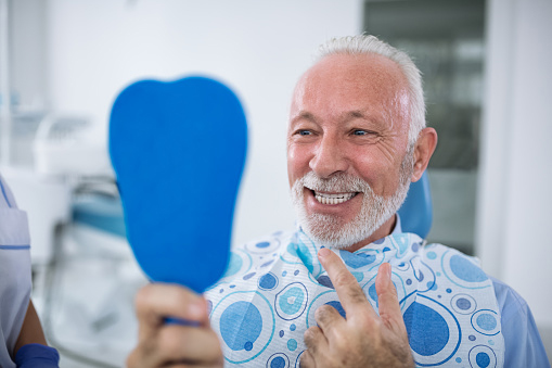  Older man smiling in handheld mirror at Martin Periodontics in Mason,  