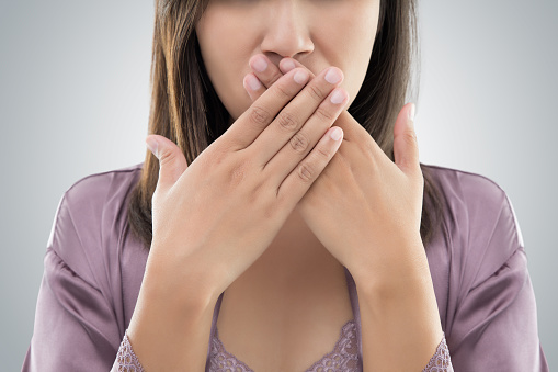 A woman holding hands over her mouth because of bad breath at Martin Periodontics in Mason, OH